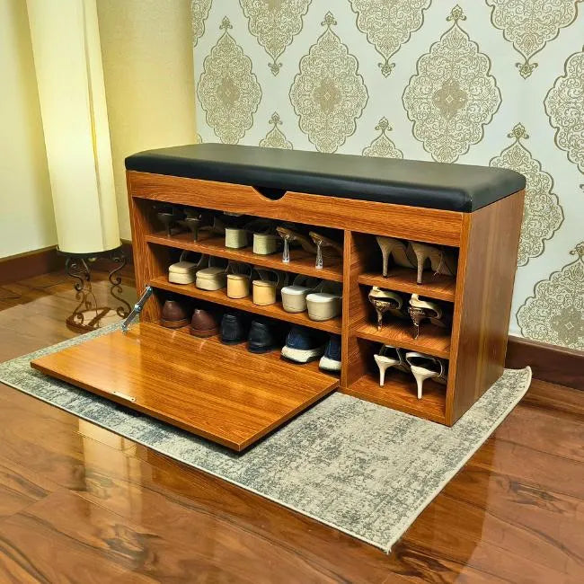 Wooden shoe rack cabinet with black cushioned top in a room with patterned wallpaper.