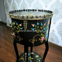 Decorative round wooden table with floral patterns and gold accents against a patterned wallpaper background.