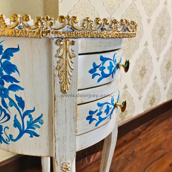 A close up shot of a white wooden table in chalk finish with blue elegant painted patterns and gold trims.