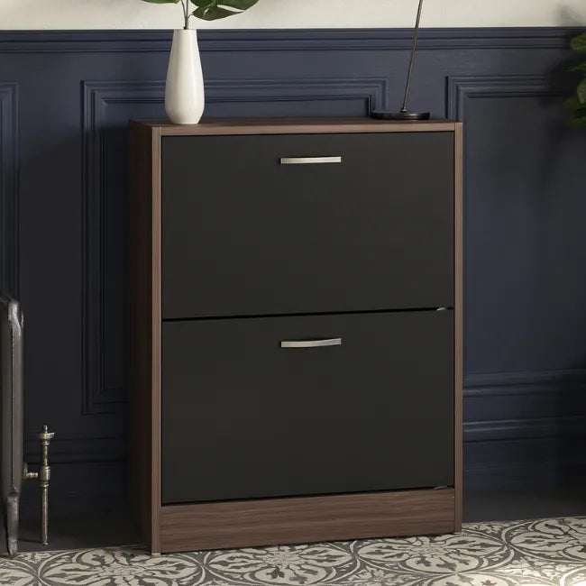 Dark wooden two-drawer shoe cabinet against a dark paneled wall.