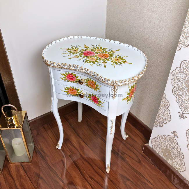 A white decorative wooden side table with painted patterns and gold trim on a wooden floor.