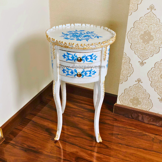 Fron view of a white decorative wooden table with painted patterns and gold trims on a wooden floor.