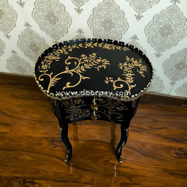 Decorative black wooden table with gold floral patterns on a wooden floor and patterned wallpaper.