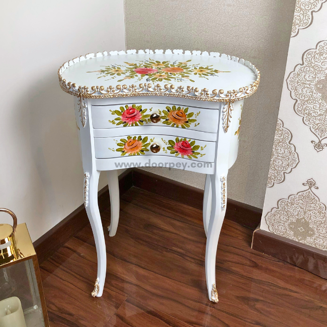 Front view of a white wooden side table with hand painted patterns and gold trims on a wooden floor.