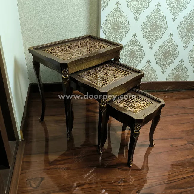 Set of three wooden nesting tables with a woven cane top on a wooden floor.