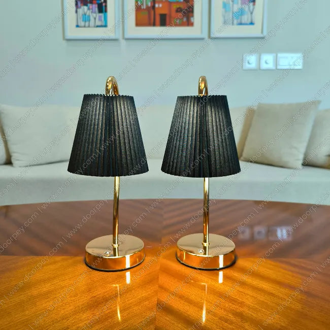Two black table lamps with gold bases on a wooden surface, with a blurred background of a living room.
