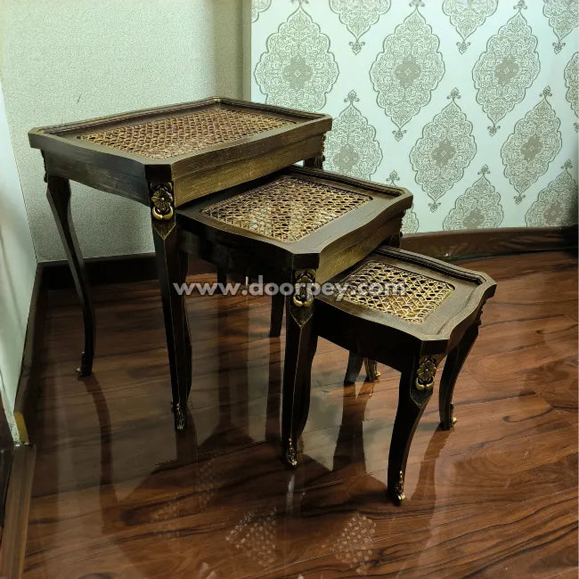 Set of three wooden nesting tables with woven cane tops on a wooden floor.