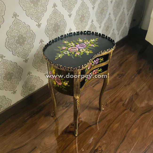 Decorative wooden end table with floral patterns on a wooden floor and patterned wallpaper.