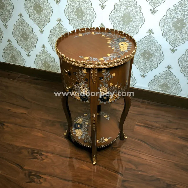 Decorative round wooden table with intricate designs on a wooden floor and patterned wallpaper.