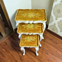 Side view of Rustic Ramble wooden nesting tables showcasing intricate floral artwork on a warm woodgrain surface with a distressed white finish.