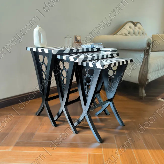 Three wooden nesting tables with black and white striped tops and black legs, styled in a living room setting.