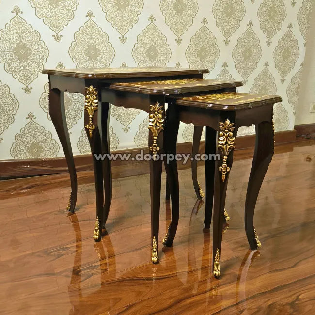 Set of three ornate wooden nesting tables with gold accents on a wooden floor.