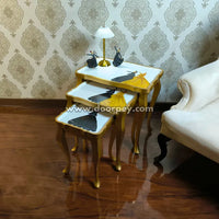 Set of three gold nesting tables with white tops in a room with patterned wallpaper and a white sofa.