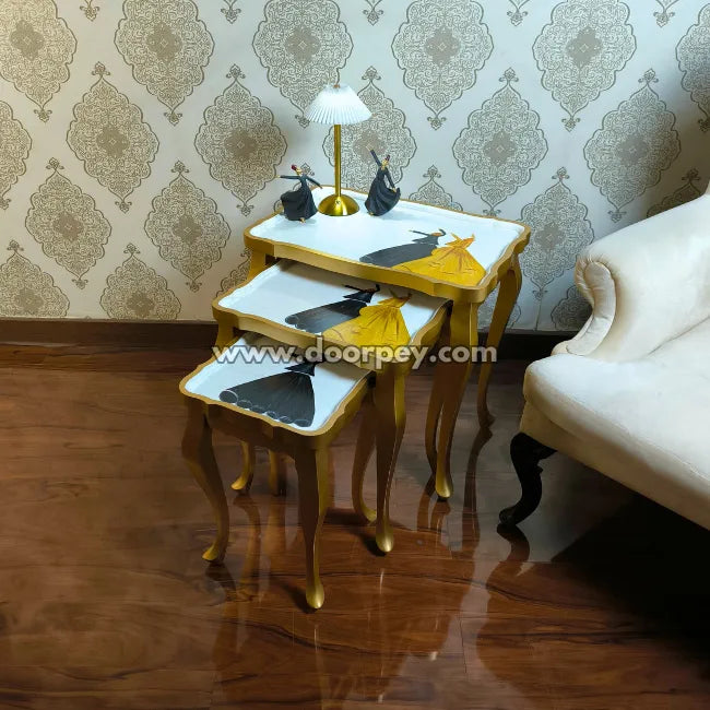 Set of three gold nesting tables with white tops in a room with patterned wallpaper and a white sofa.