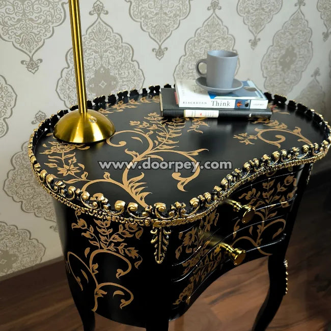 Decorative black side table with gold accents, lamp, and books against a patterned wall.