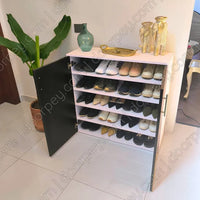A white shoe cabinet with an open black door, filled with multiple pairs of shoes, styled with decorative vases on top in a home interior.