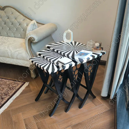 Wooden nesting tables with black and white striped spiral-patterned styled in a living room next to a tufted sofa.