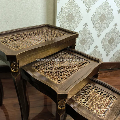 Set of three cane woven wooden nesting tables against a decorative wallpaper background