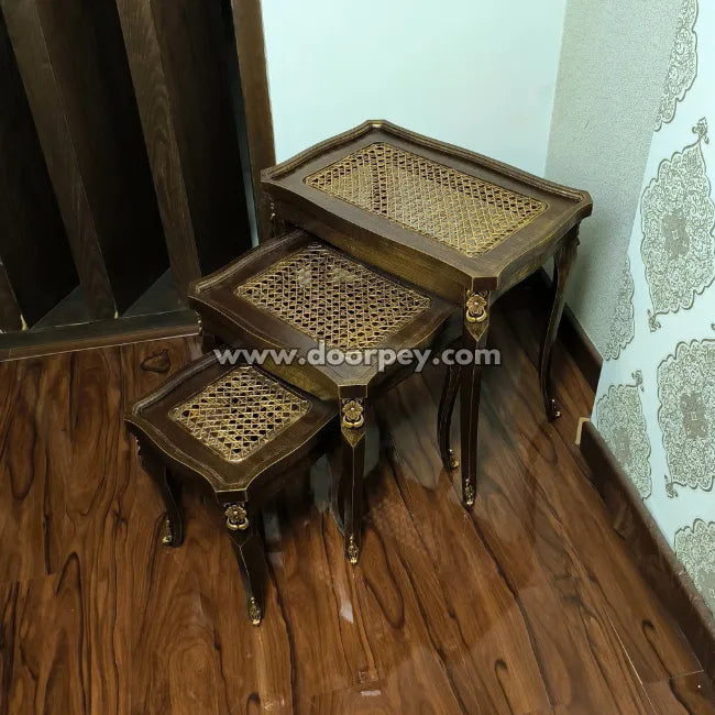 Set of three wooden nesting tables with wicker tops on a wooden floor.