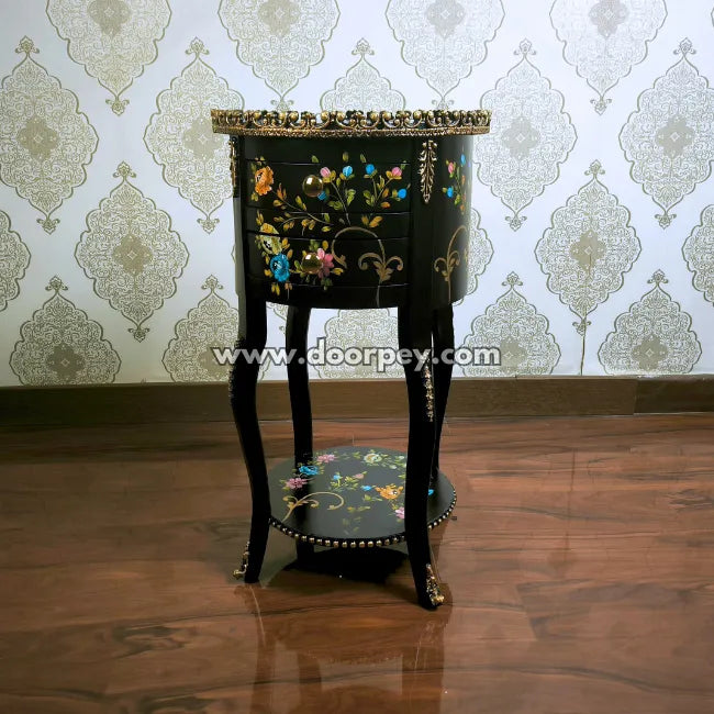 Decorative black woodene end table with floral designs against a patterned wallpaper background