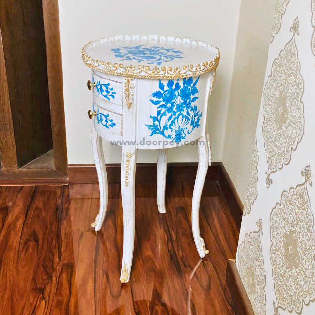 Side profile of a white round wooden side table with blue painted patterns and gold trims.