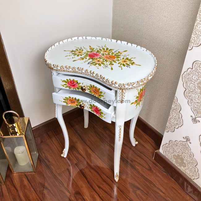 A white wooden side table with hand painted patterns and gold trims. The table has its two drawers open.