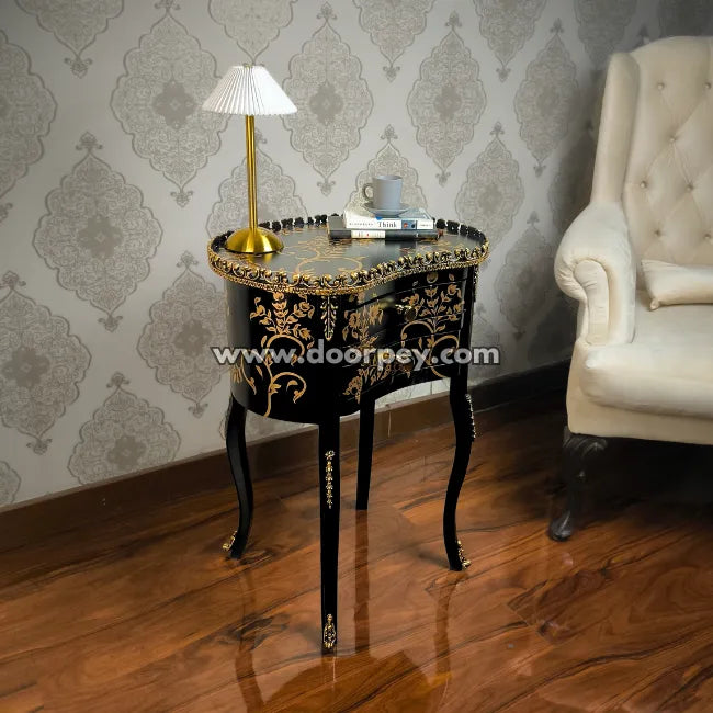 Decorative wooden side table with gold accents in a room with patterned wallpaper and a white armchair.