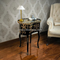 Decorative wooden side table with gold accents in a room with patterned wallpaper and a white armchair.