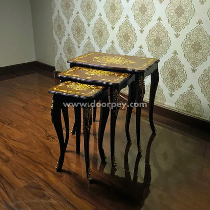 Set of three nested wooden tables with hand painting against a patterned wallpaper background