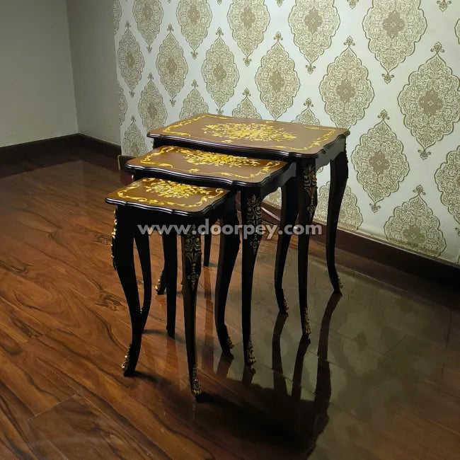 Set of three nested wooden tables with hand painting against a patterned wallpaper background