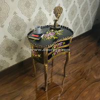 Decorative wooden side table with floral patterns and gold accents against a patterned wall.