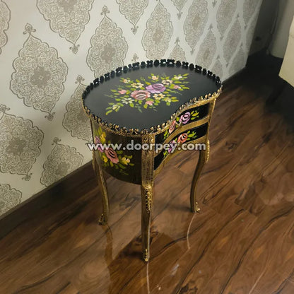 Decorative wooden end table with floral patterns on a wooden floor and patterned wallpaper.