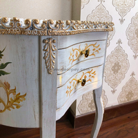 Close up image of a white wooden table with painted patterns and gold trims.