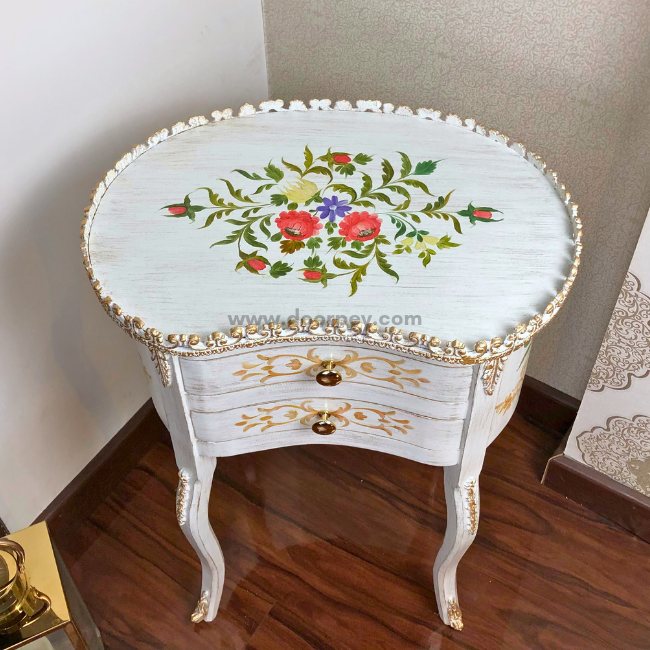 Top view of a white wooden side table with colorful painted patterns and gold trim on a wooden floor