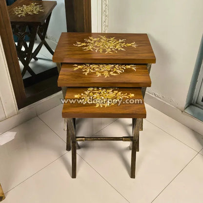 Set of three brown handpainted wooden nesting tables on a tiled floor.