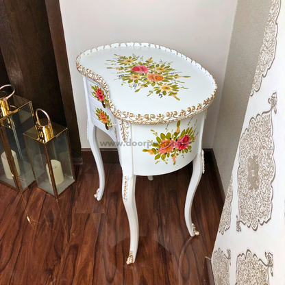 Side angle of a white wooden side table with colorful painted patterns and gold trims.