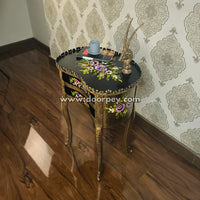 Decorative wooden end table with floral designs on a wooden floor and patterned wallpaper.