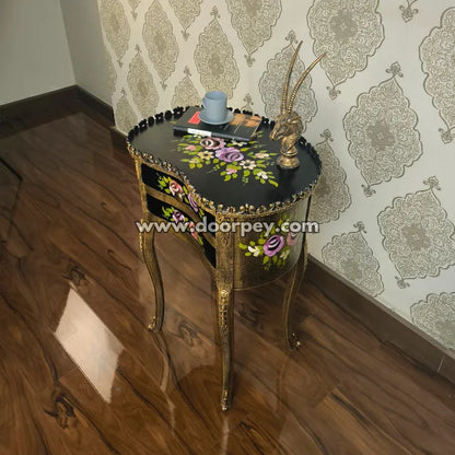 Decorative wooden end table with floral designs on a wooden floor and patterned wallpaper.