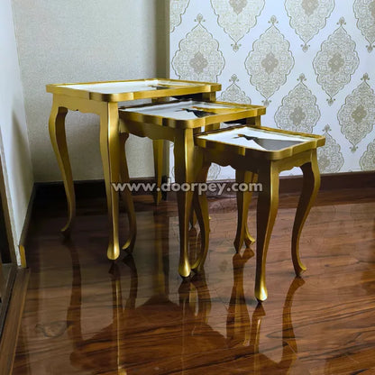 Set of gold nesting tables against a decorative wall.