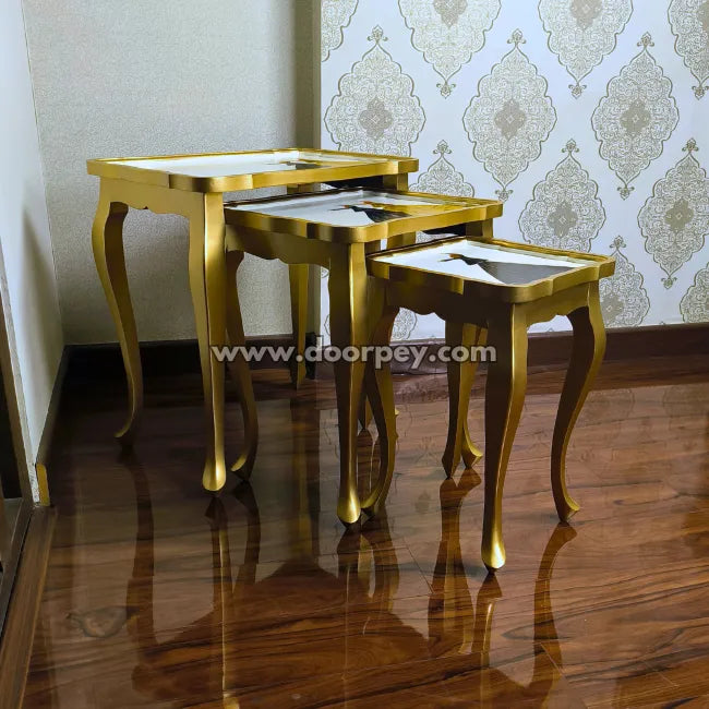 Set of gold nesting tables against a decorative wall.