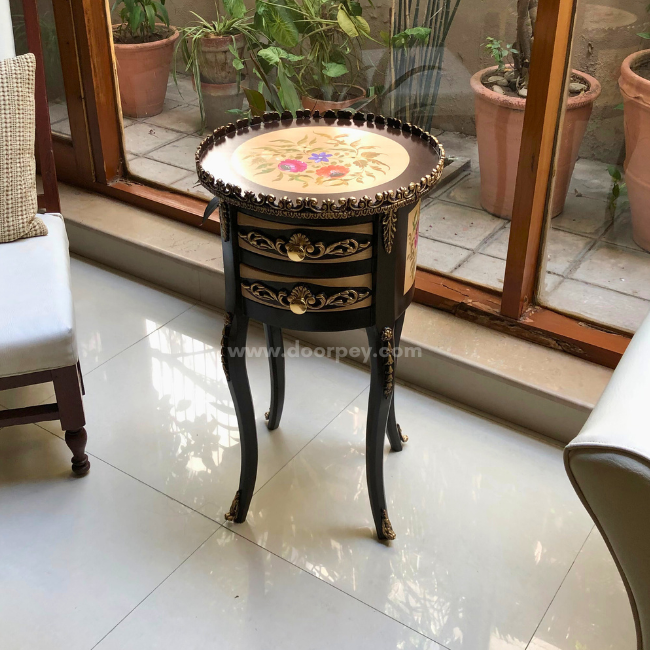 Elevated view of a hand painted wooden side table next to a chair on a tiled floor