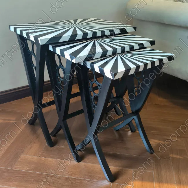 Three wooden nesting side tables with black and white striped starburst-patterned tops and black legs, shown on a wooden floor in a room setting.