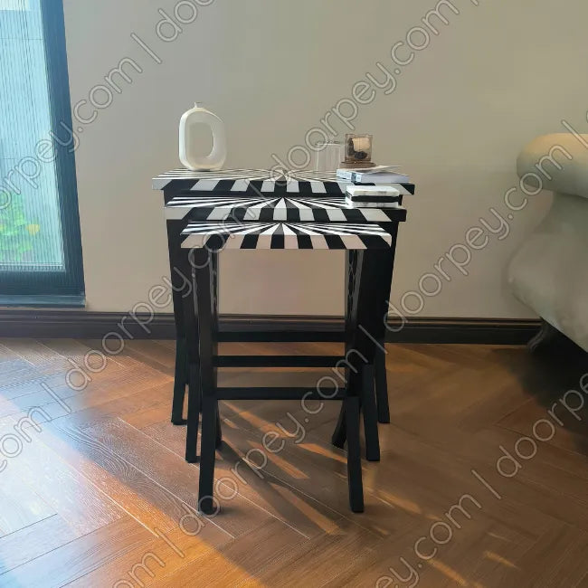 A set of three nested side tables with striped black and white wavy-patterned tops, shown in a home interior setting with a wooden floor and a window.