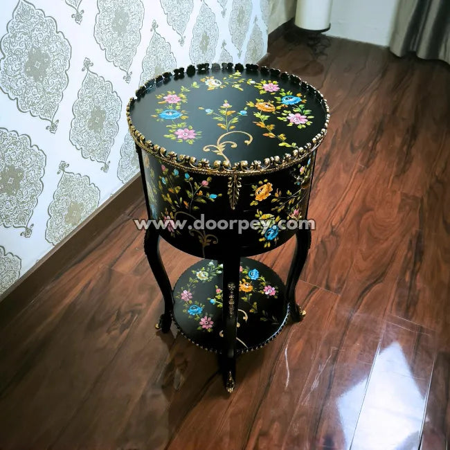 Decorative round wooden side table with hand painted floral patterns on a wooden floor.