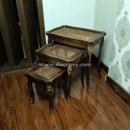 Set of three wooden nesting tables with cane woven tops on a wooden floor.