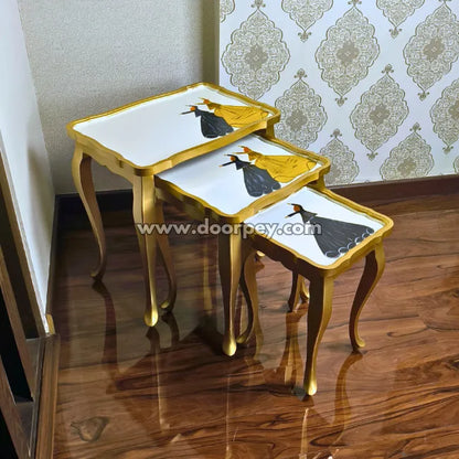 Set of three wooden nesting tables with gold frames and artistic designs on a wooden floor.