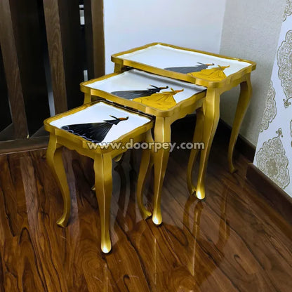 Set of three wooden nesti tables with gold legs and white tops on a wooden floor.