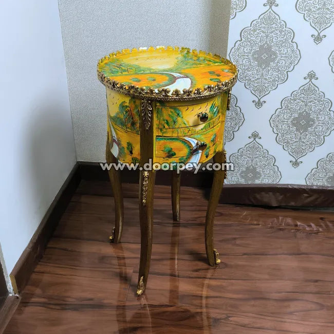 Hand painetd round side table with gold accents and colorful design against a patterned wallpaper background.