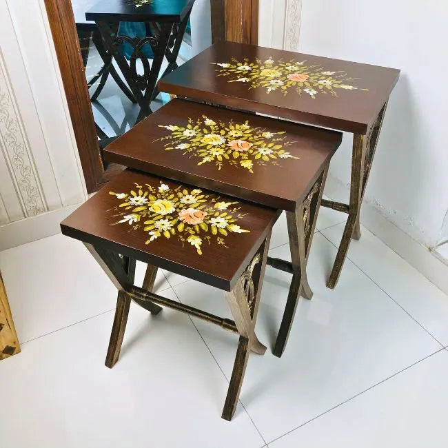 Space-saving Woodland Wonders nesting tables stacked neatly, featuring a rich brown finish with hand-painted floral detailing