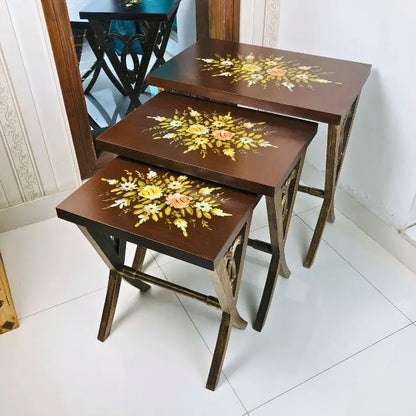 Space-saving Woodland Wonders nesting tables stacked neatly, featuring a rich brown finish with hand-painted floral detailing
